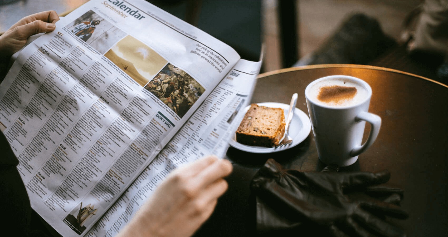 Person reading a newspaper with food and coffee